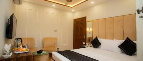 Una habitación de hotel con cama, escritorio, silla, una mesita y ventilador de techo.