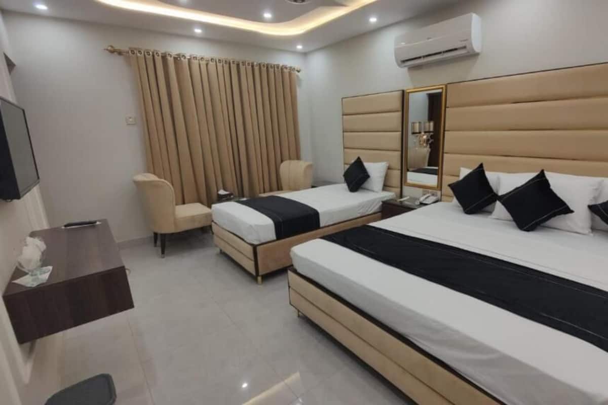 A hotel room with two beds, a desk, a chair, a TV, and an air conditioning unit.