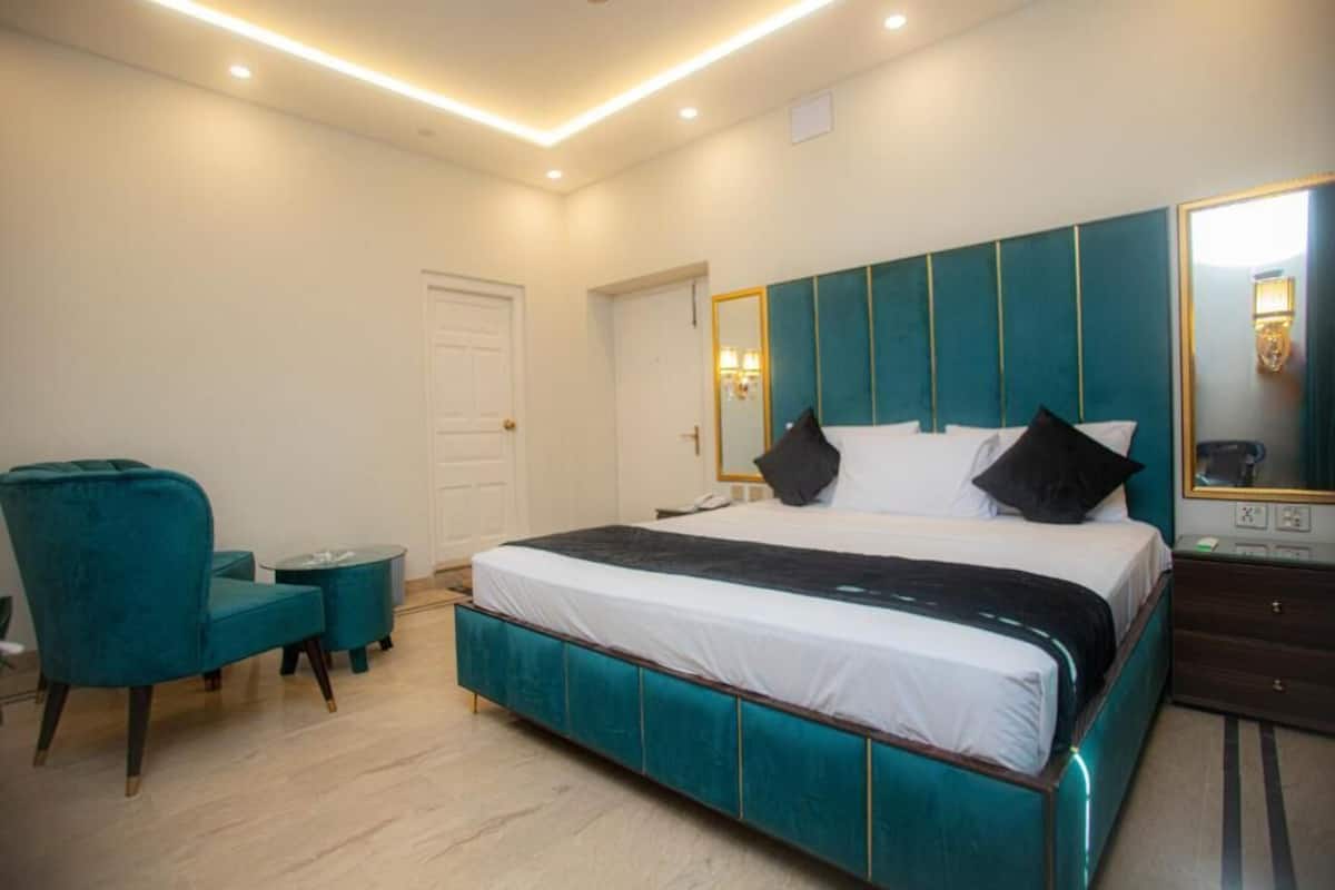 A modern bedroom with a teal upholstered bed, a matching armchair, and a bedside table.
