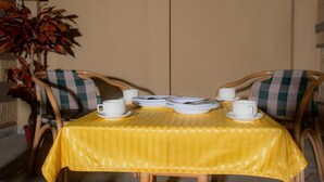 Une table à manger recouverte d’une nappe jaune, avec des assiettes et des tasses blanches, entourée de chaises à motifs à carreaux.