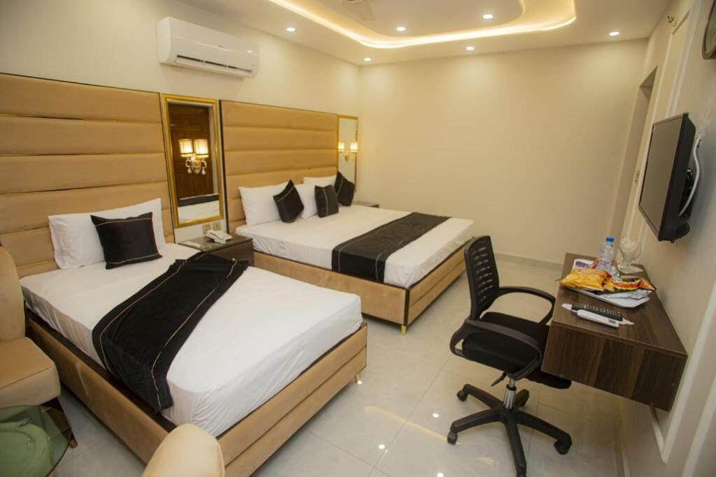 A hotel room with two beds, a desk, a chair, a TV, and a mirror.