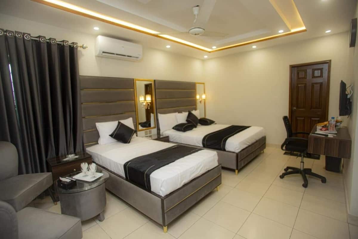 A hotel room with two beds, a desk, a chair, and a small table.