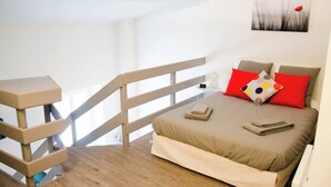 A bedroom with a bed, pillows, a bedside table, a nightstand, and a painting on the wall.