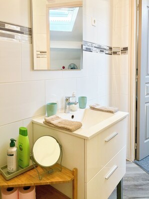 A bathroom with a white sink, a mirror, a towel, and toiletries on the countertop. - Cozy Duplex in Bordeaux,  peaceful and inviting ! (BORDEAUX)