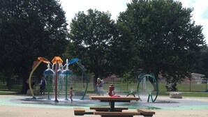 Un parque con zona de juegos acuáticos, mesas de picnic y bancos.