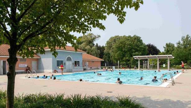 Una piscina pública con gente nadando y tomando el sol.