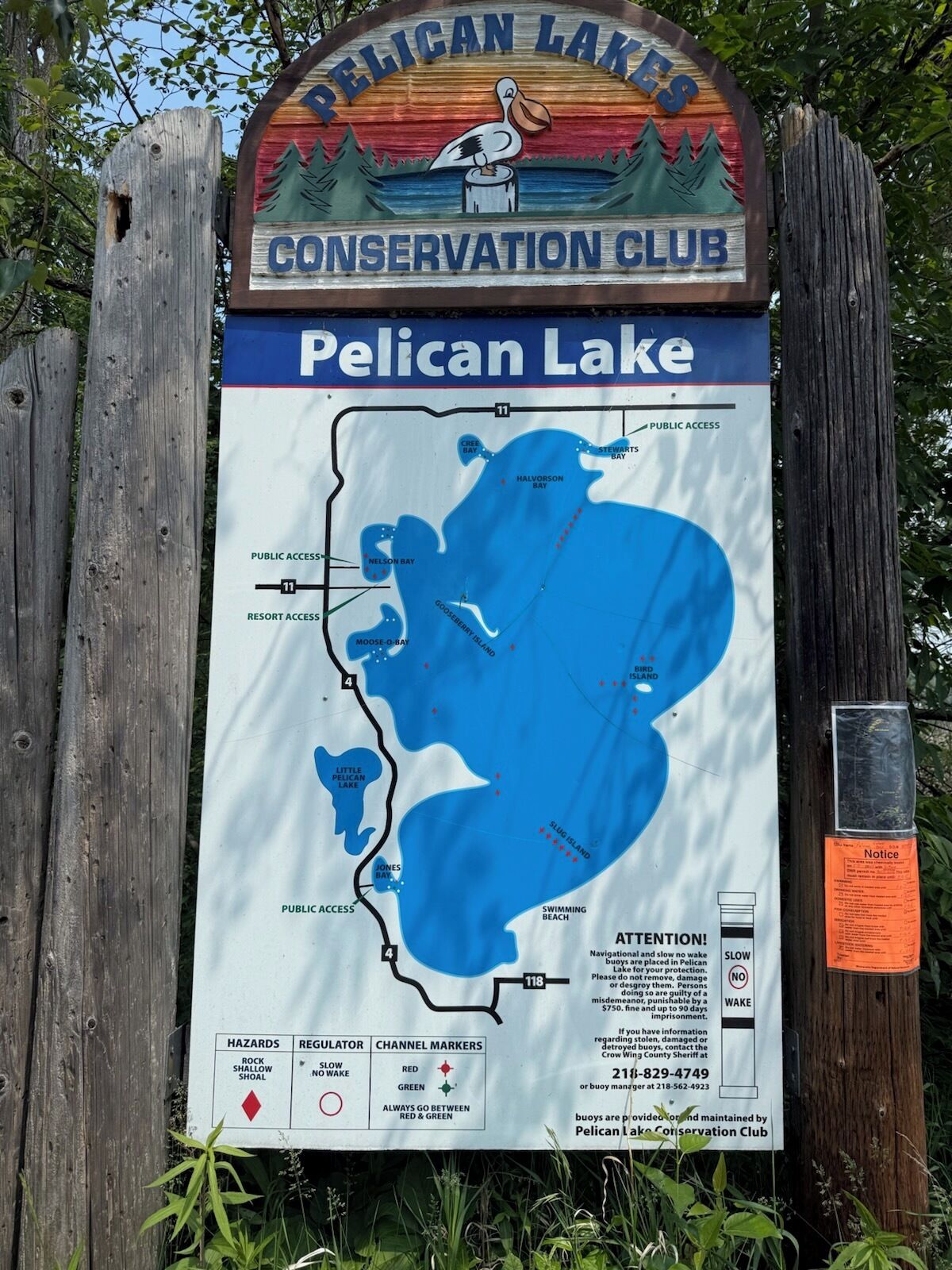 A wooden sign for Pelican Lake Conservation Club with a map of the lake and its bays, marked trails, and public access points.