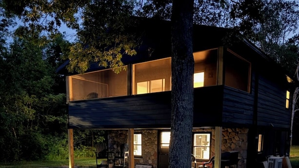 Une maison moderne à deux étages, dotée d’une façade en pierre, de grandes fenêtres et d’un jardin bien entretenu agrémenté de rochers et de plantes en pot.