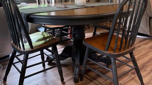 Un coin repas comprenant une table ronde, quatre chaises, un ventilateur de plafond et un mur en pierre agrémenté d’une étagère.