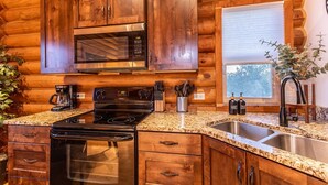 Eine Küchenzeile im Holzblockhaus-Stil mit Holdekor-Schränken, einer Edelstahl-Spüle, einer Mikrowelle, einem Herd und einer Kaffeemaschine.