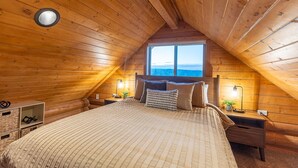 Ein gemütliches Schlafzimmer im Dachgeschoss mit einem großen Bett, Holzwänden und einem Fenster mit Blick.