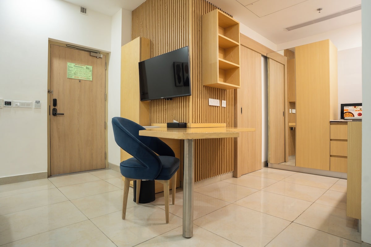 A modern room with a wooden panel wall, a flat-screen TV mounted above a table, a blue chair, and a wooden cabinet with a shelf.