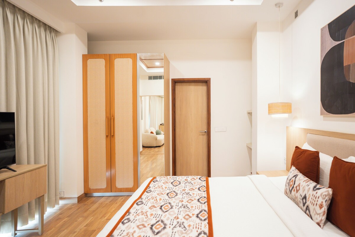 A hotel room with a bed, a desk, a TV, a wardrobe, and a sofa in the background.