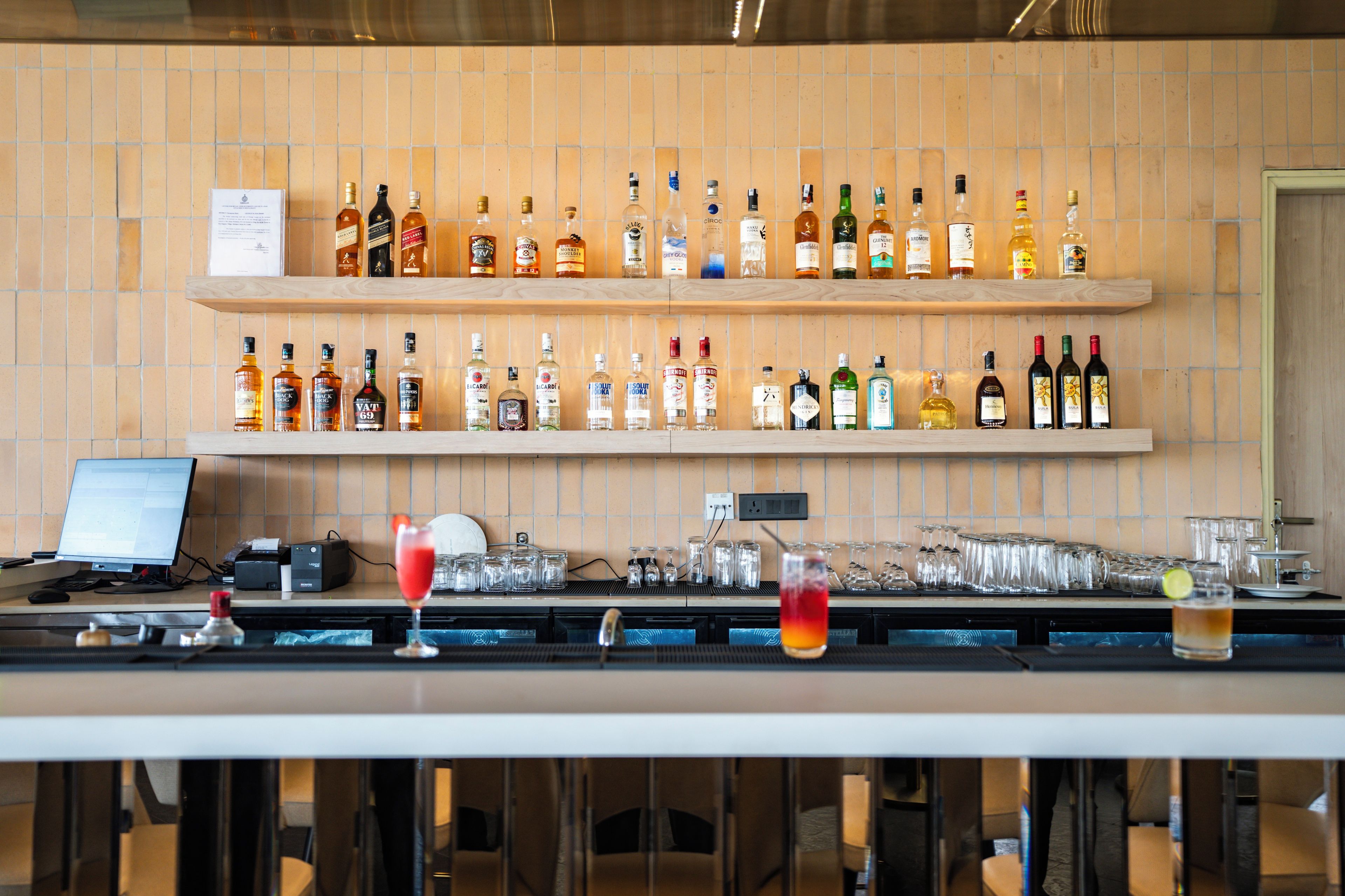 A bar area with shelves of liquor bottles, glasses, and a computer monitor.
