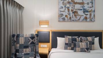 A hotel room with a bed, a nightstand, a lamp, a chair, and a wall art piece.