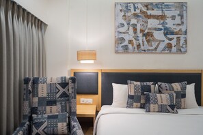 A hotel room with a bed, a nightstand, a lamp, a chair, and a wall art piece. - AR Suites KLJ Square (Gurugram)