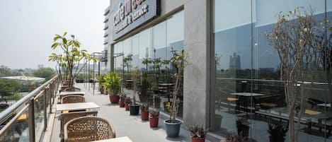 A café with outdoor seating, potted plants, and a view of the cityscape.