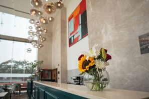 A restaurant interior with a clear view of the dining area, a vase with flowers on the counter, and a modern light fixture. - AR Suites KLJ Square (Gurugram)
