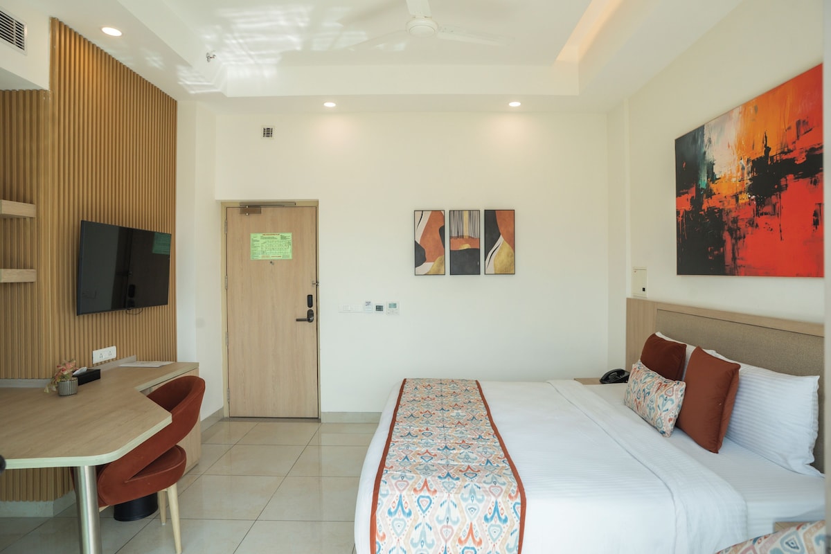 A hotel room with a bed, a desk, a chair, a television, and artwork on the wall.