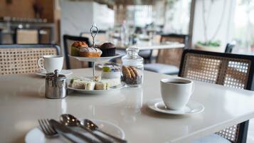 Una mesa dispuesta para una comida con varios sándwiches, un muffin, un tarro de galletas, una taza de café y una tetera.