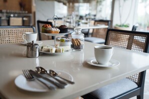 A table set for a meal with a variety of sandwiches, a muffin, a jar of cookies, a coffee cup, and a teapot. - AR Suites KLJ Square (Gurugram)