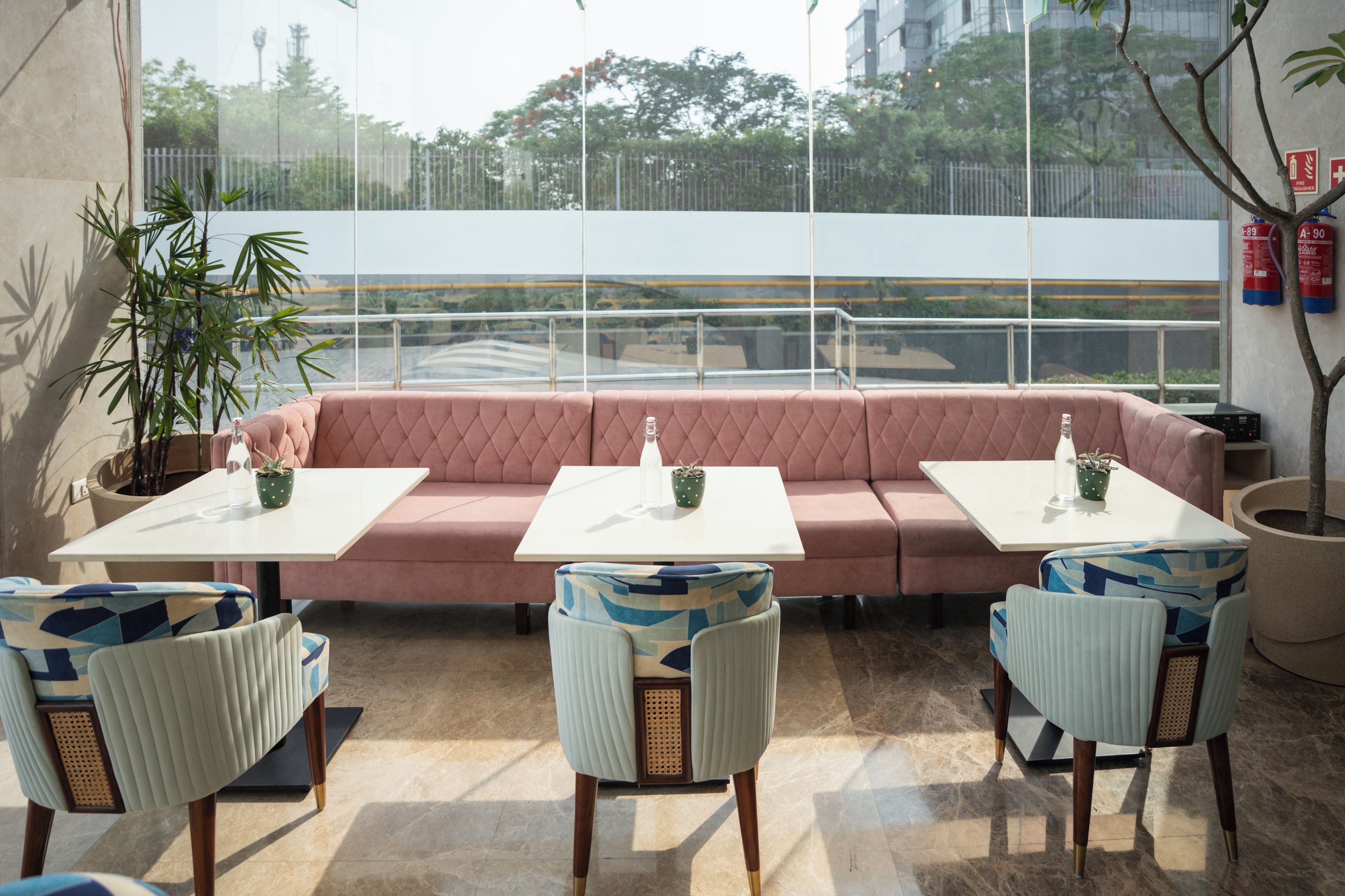 Un área de estar moderna al aire libre con un sofá rosa, mesas blancas y sillas estampadas.