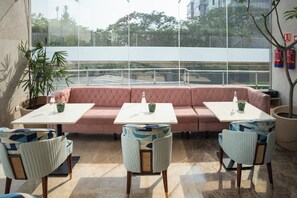 A modern outdoor seating area with a pink sofa, white tables, and patterned chairs. - AR Suites KLJ Square (Gurugram)