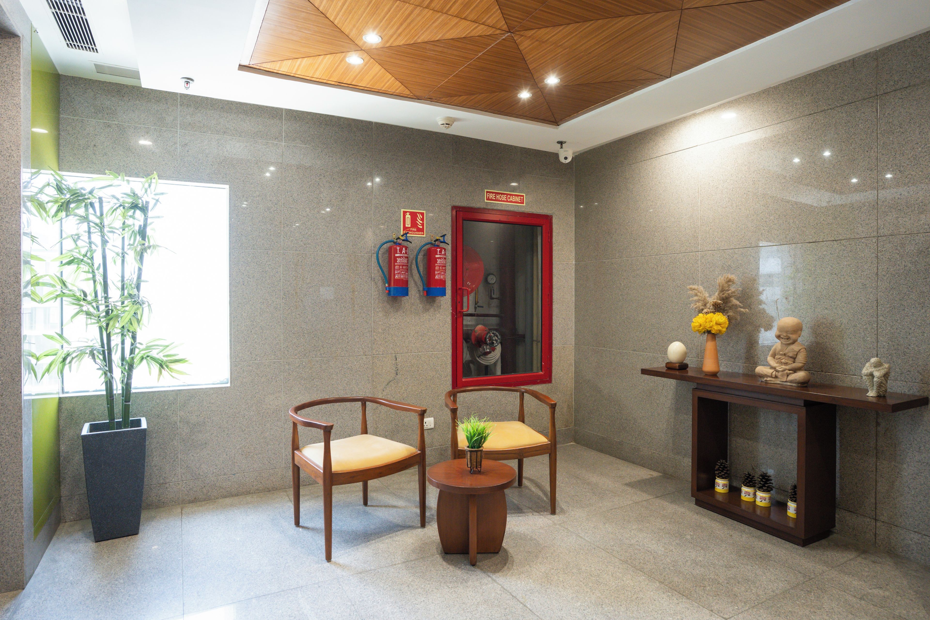 Eine moderne Lobby mit zwei Holzstühlen, einem kleinen runden Tisch, einem Brandschutzschrank und einem großen Spiegel.