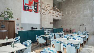 A modern restaurant with teal and white decor, multiple tables and chairs, and a central bar area.