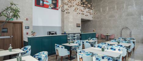 Un restaurant moderne, décoré dans des tons de turquoise et de blanc, avec de nombreuses tables et chaises, et un bar central.