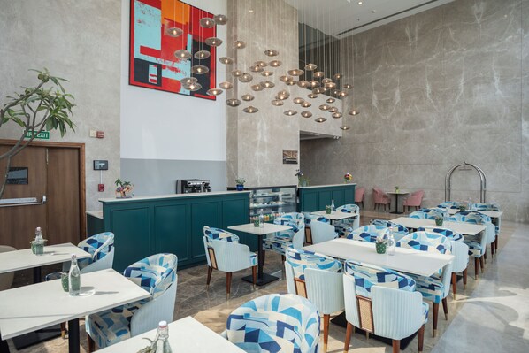 A modern restaurant with teal and white decor, multiple tables and chairs, and a central bar area. - AR Suites KLJ Square (Gurugram)