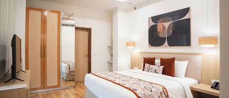 A modern hotel room with a large bed, wooden wardrobe, ceiling fan, and abstract artwork.