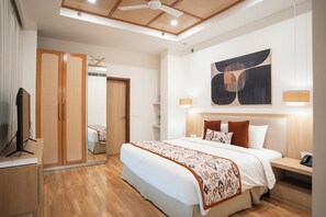 A modern hotel room with a large bed, wooden wardrobe, ceiling fan, and abstract artwork. - AR Suites KLJ Square (Gurugram)