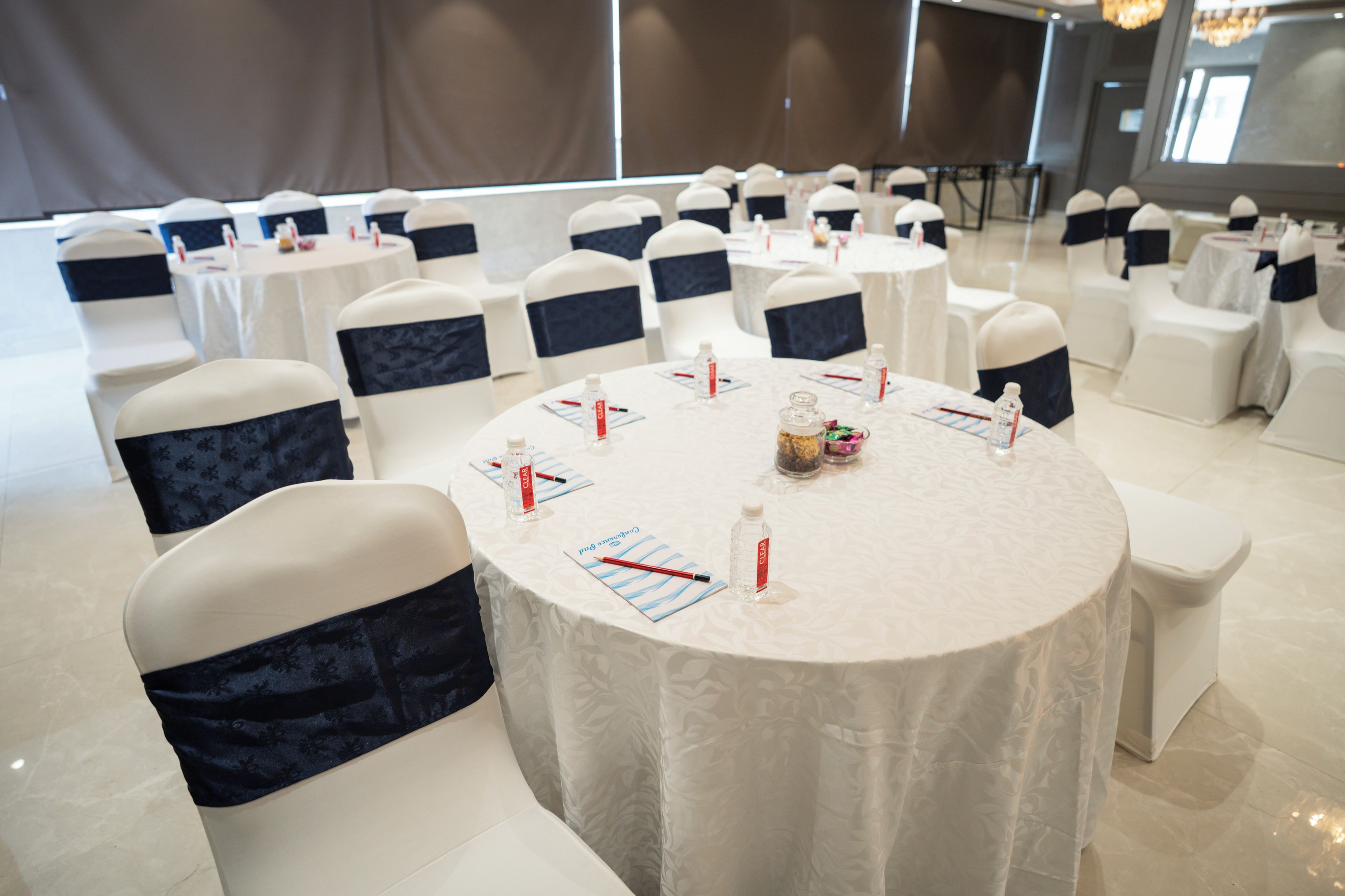 A conference room with round tables, white chairs with navy blue sashes, and a white tablecloth.