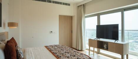 A bedroom with a bed, a television on a stand, a window with a view, and a ceiling with a wooden design.