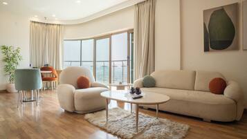 Una sala de estar moderna con sofá, sillón, mesa de centro y un amplio ventanal con cortinas.
