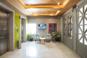 A lobby with a modern design, featuring a reception desk, seating area, and a television screen. - AR Suites KLJ Square (Gurugram)