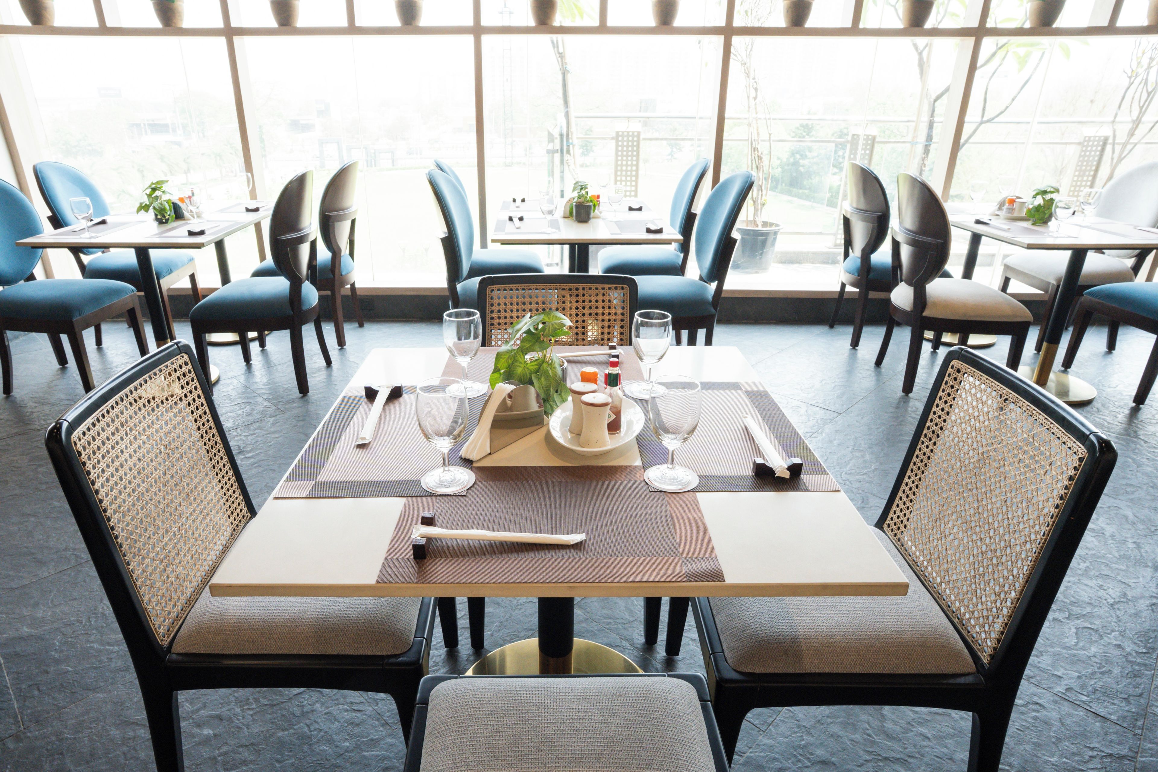 Un restaurante con un interior moderno, que presenta una mesa central para comer con sillas, un gran ventanal que proporciona luz natural y vistas al exterior.