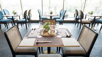 Un restaurante con un interior moderno, que presenta una mesa central para comer con sillas, un gran ventanal que proporciona luz natural y vistas al exterior.