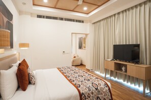 A modern hotel room with a large bed, a television on a wooden stand, and a view of the city through the window. - AR Suites KLJ Square (Gurugram)