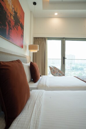 Habitación de hotel con dos camas, un ventanal con vistas, una lámpara en el techo y un cuadro en la pared.
