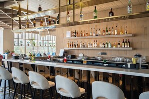 A bar area with multiple liquor bottles, glasses, and stools. - AR Suites KLJ Square (Gurugram)
