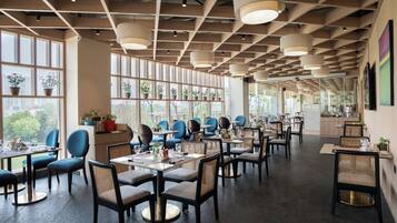 Un restaurante moderno con techos altos, ventanas amplias y diversas opciones de asientos, incluyendo mesas y sillas.
