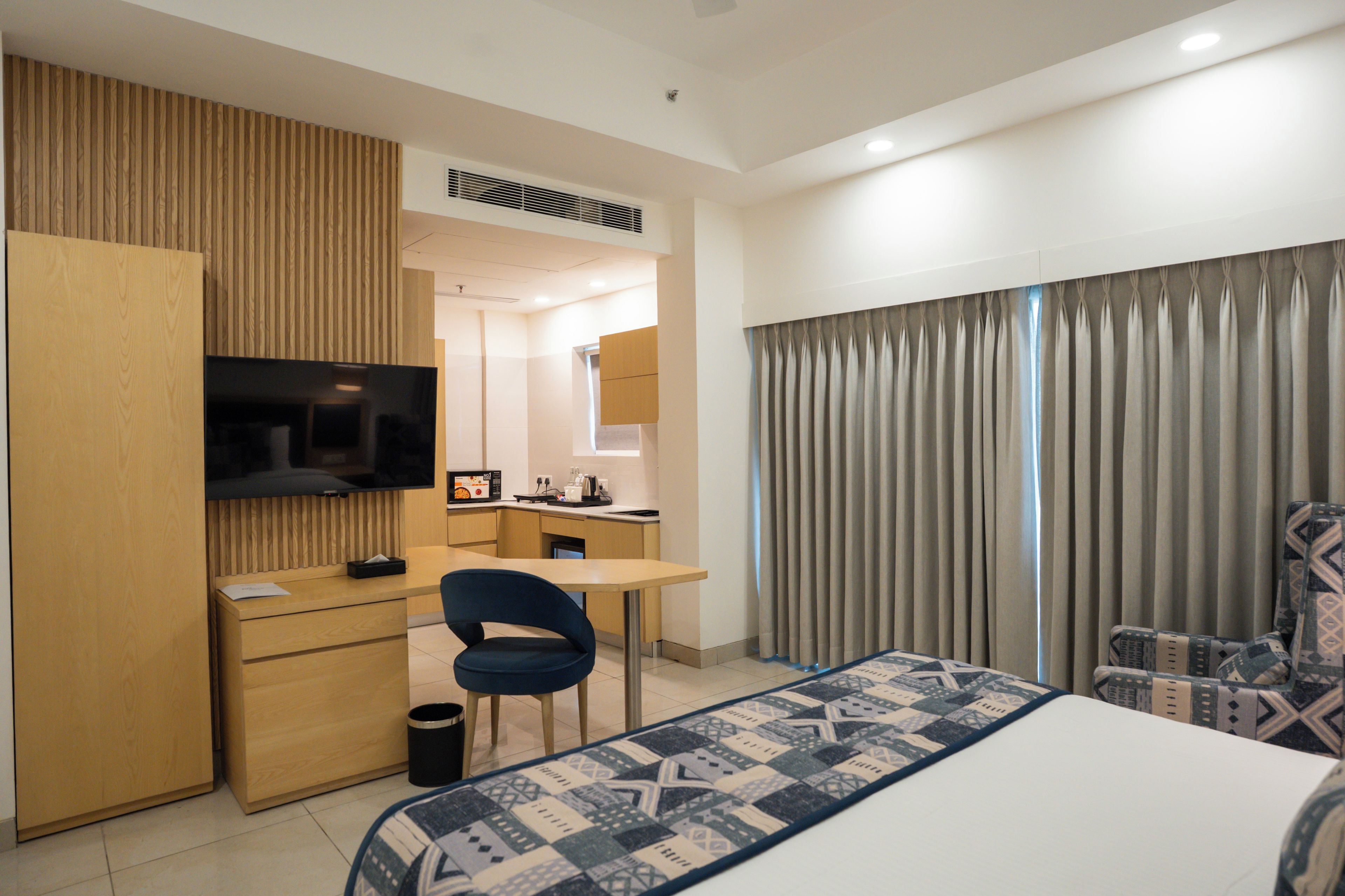 A hotel room with a bed, a desk, a chair, a television, and a bathroom visible through an open door.