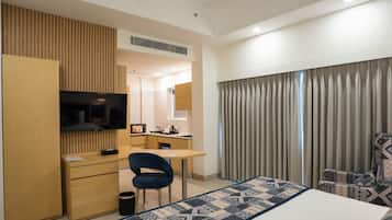 Habitación de hotel con cama, escritorio, silla, televisor y baño visible a través de una puerta abierta.