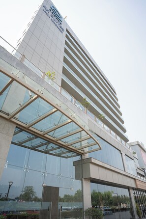 A modern building with a glass facade and a prominent sign. - AR Suites KLJ Square (Gurugram)