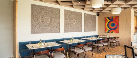Un restaurante con cabinas y mesas, vigas de madera en el techo y decoración mural con diseños.
