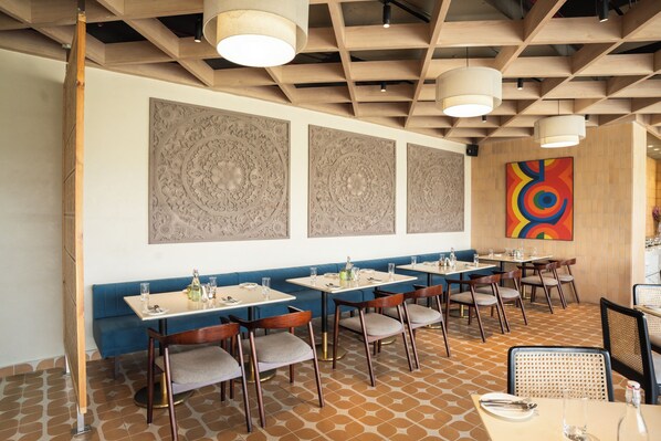 A restaurant with booths and tables, wooden ceiling beams, and patterned wall decor. - AR Suites KLJ Square (Gurugram)