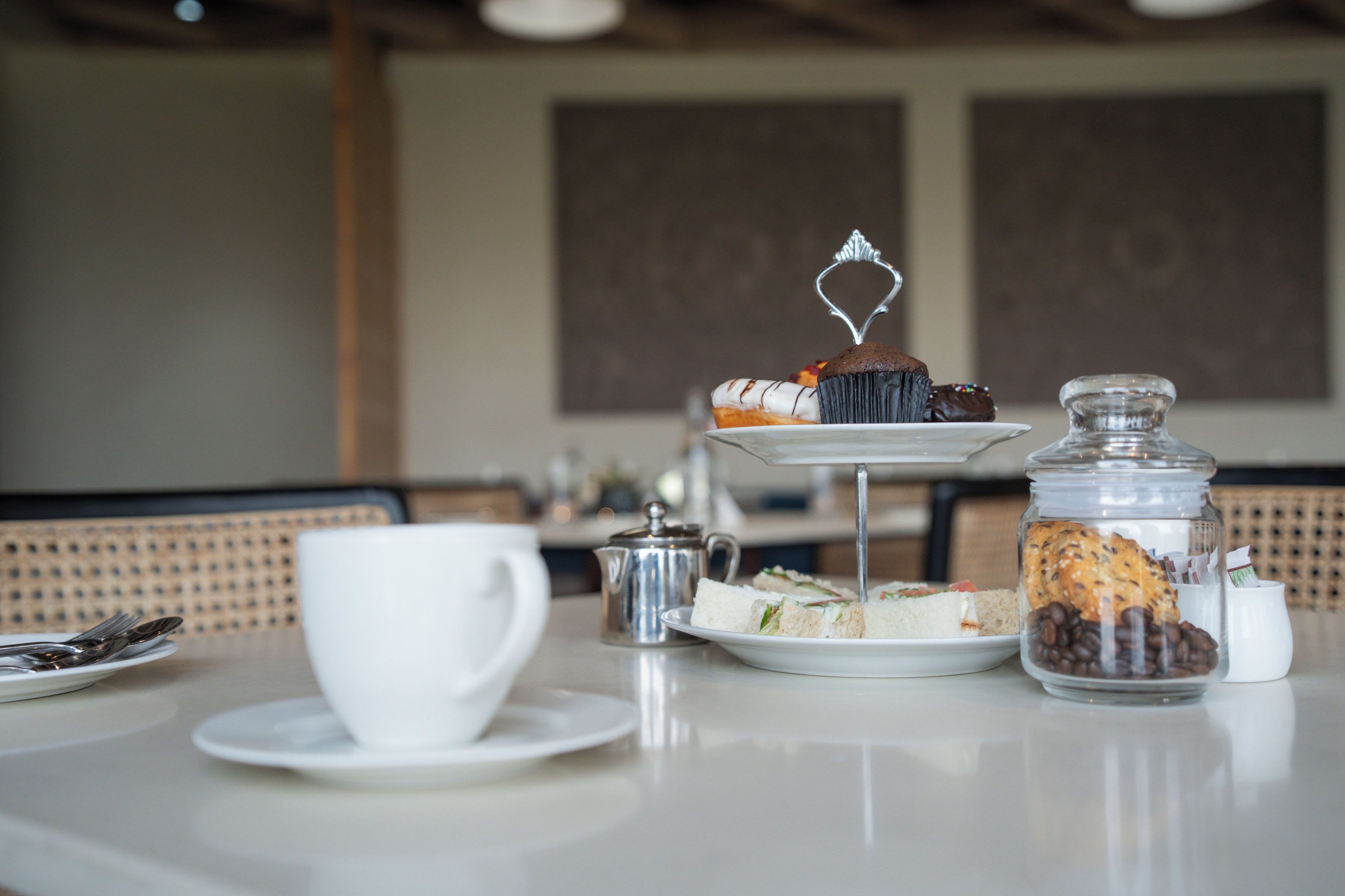 A table with a white cup, a silver teapot, and a glass jar filled with cookies.