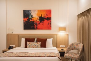 A hotel room with a large bed, a chair, a bedside table with a lamp, and a painting on the wall.